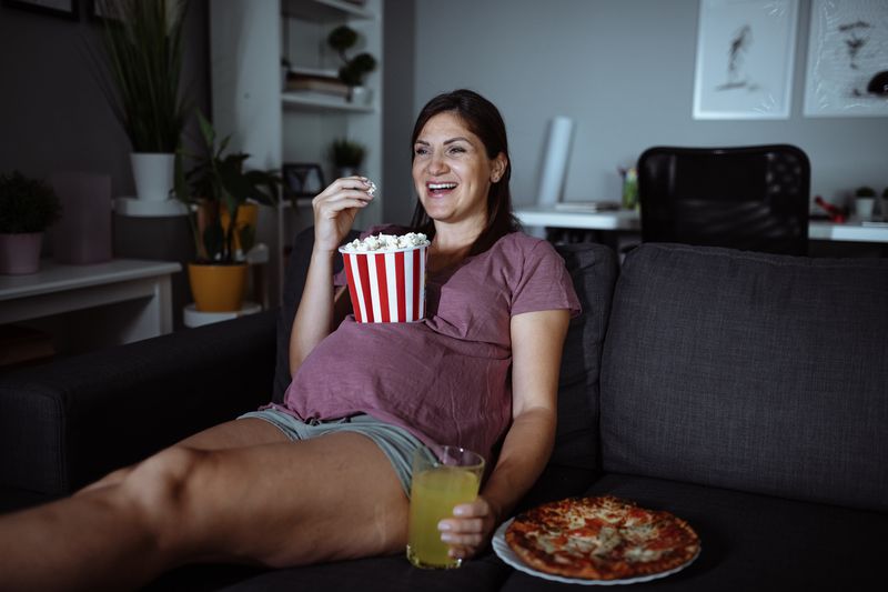 Une femme enceinte mange du pop-corn en regardant un film.