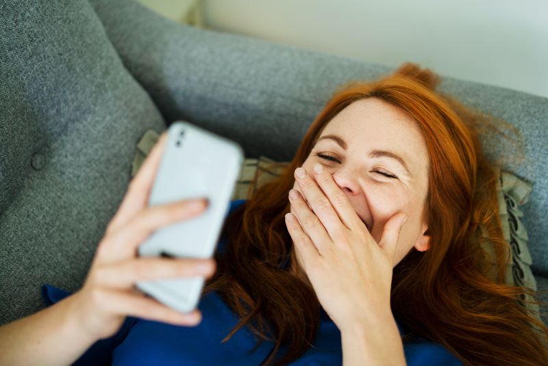 Une femme rigole en lisant un téléphone.