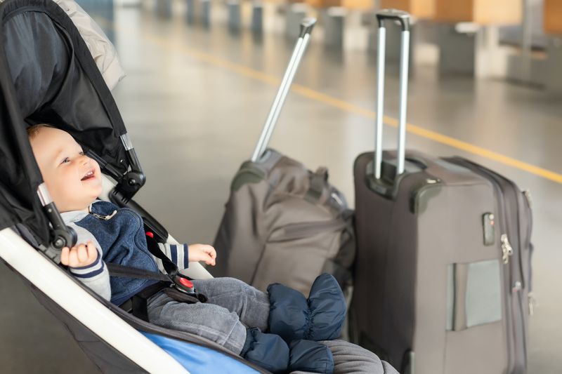 Mignon petit garçon caucasien drôle assis dans la poussette près des bagages au terminal de l