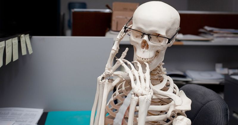 Squelette drôle assis au bureau - blagues et jeux de mots squelettes.
