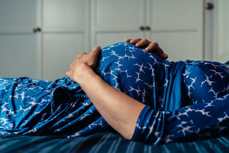 Une femme enceinte portant une chemise de nuit est allongée sur un lit avec sa main sur son ventre